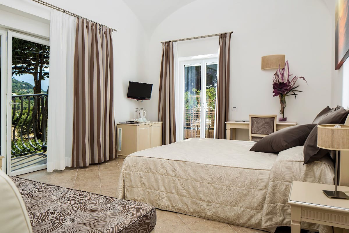 A hotel room with a large bed, a television, a desk with a lamp, and a view of the outdoors.