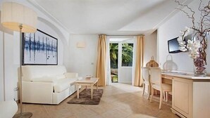A modern living room with a white sofa, a small table, a desk with a chair, a TV, and a large window with curtains. - Villa Ceselle (Anacapri)