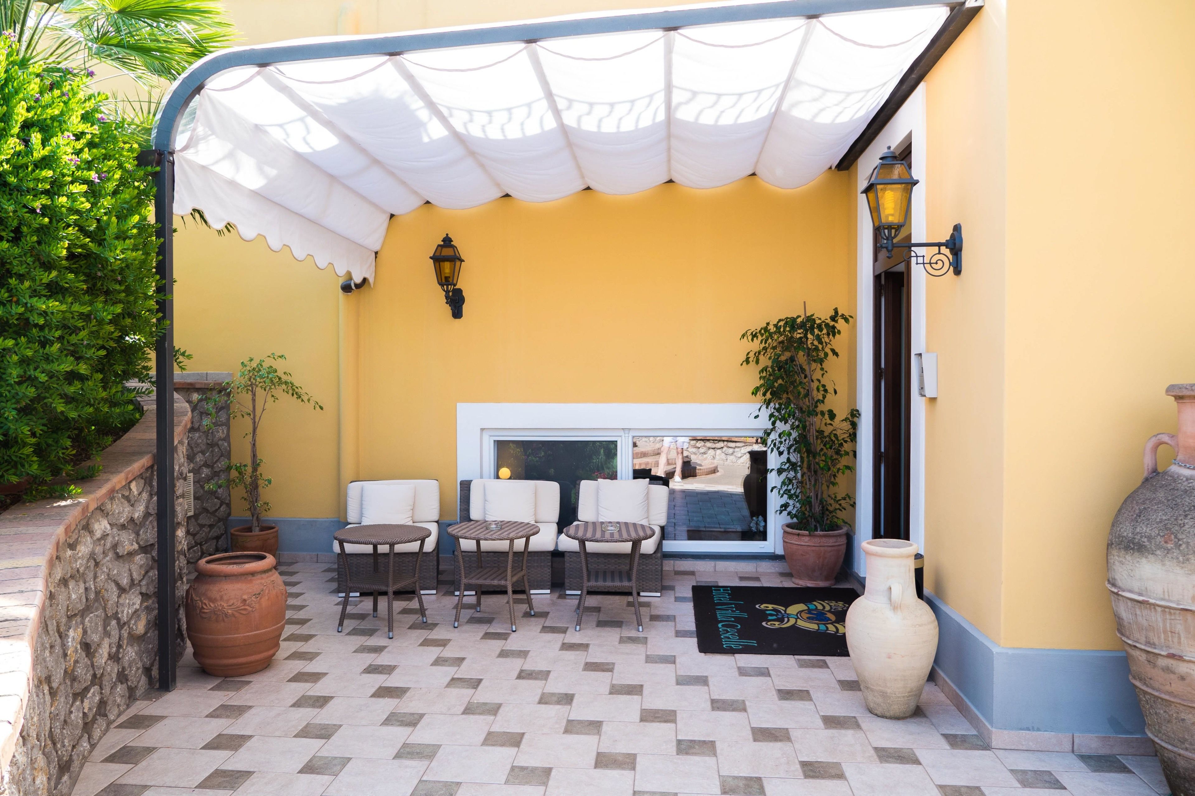 Un área de estar al aire libre con un patio cubierto, pared de piedra y plantas en macetas.