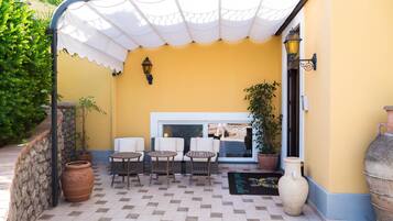 Un área de estar al aire libre con un patio cubierto, pared de piedra y plantas en macetas.