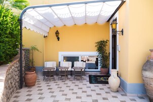 Un área de estar al aire libre con un patio cubierto, pared de piedra y plantas en macetas.