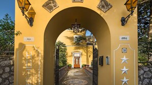 An archway leading to a hotel entrance with a yellow facade, a wooden door, and decorative lanterns. - Villa Ceselle (Anacapri)