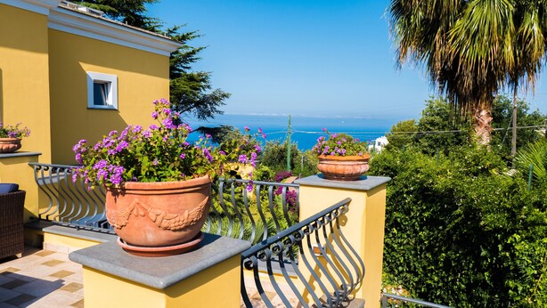 A balcony with terracotta planters, a wicker chair, and a view of the sea. - Villa Ceselle (Anacapri)