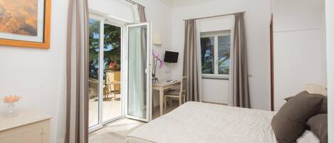 Un dormitorio con cama, escritorio, silla, televisor y puerta corrediza de vidrio que da a un espacio exterior.
