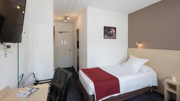 Quarto de hotel com cama, escrivaninha com cadeira, televisão fixada na parede e mesa de cabeceira pequena.