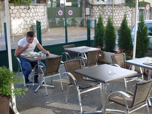 An outdoor cafe with metal tables and wicker chairs, a stone wall, and a gate with a sign. - Hôtel Les Afforêts (La Roche-sur-Foron)