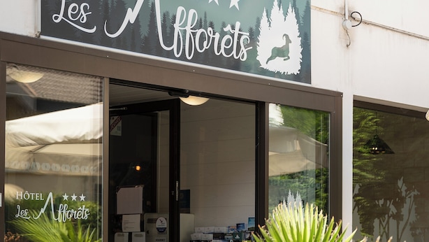 Exterior do HOTEL Les Maffrettes, com placa, entrada e área de estar ao ar livre.