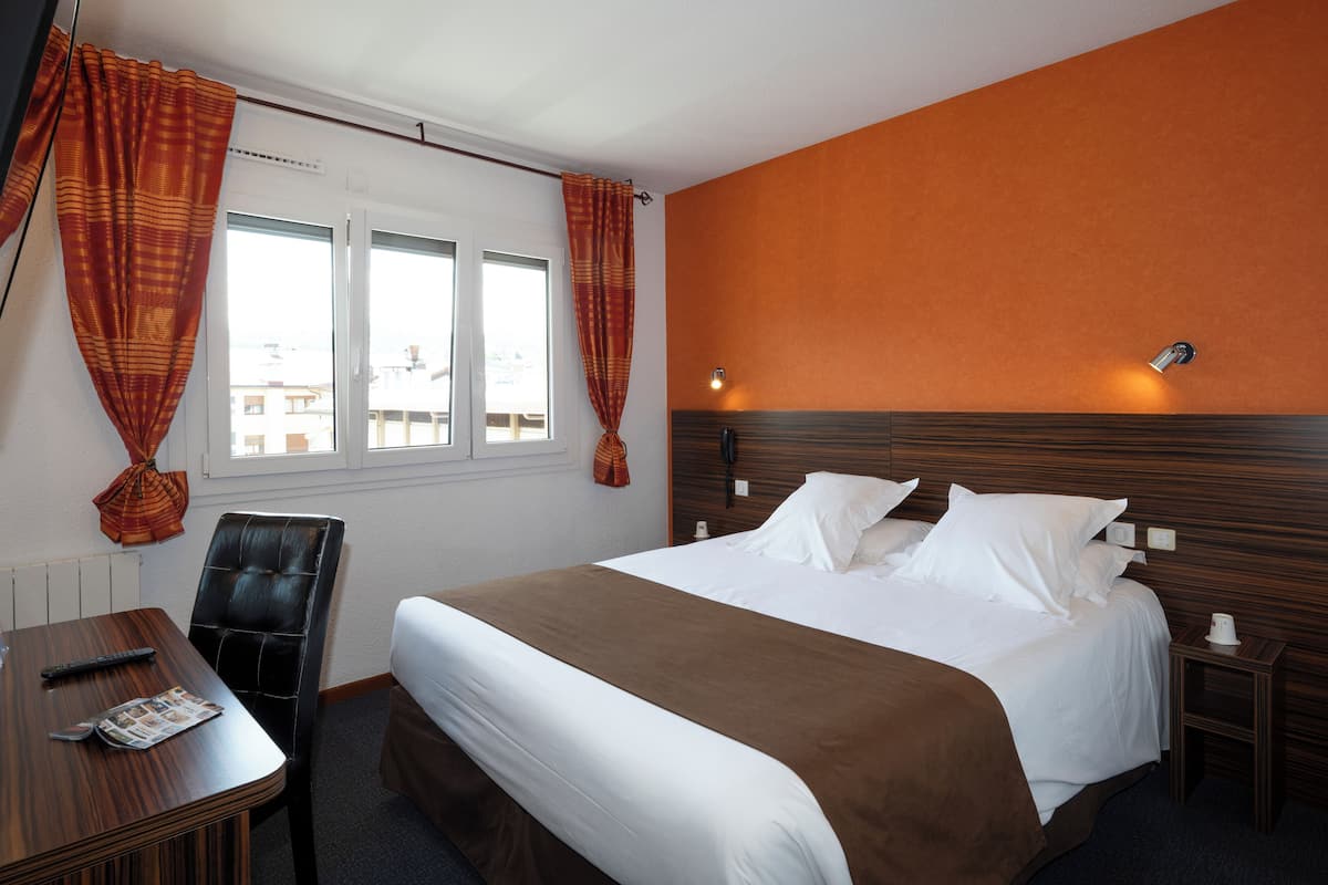 Habitación de hotel con cama, escritorio, silla y ventana con cortinas.