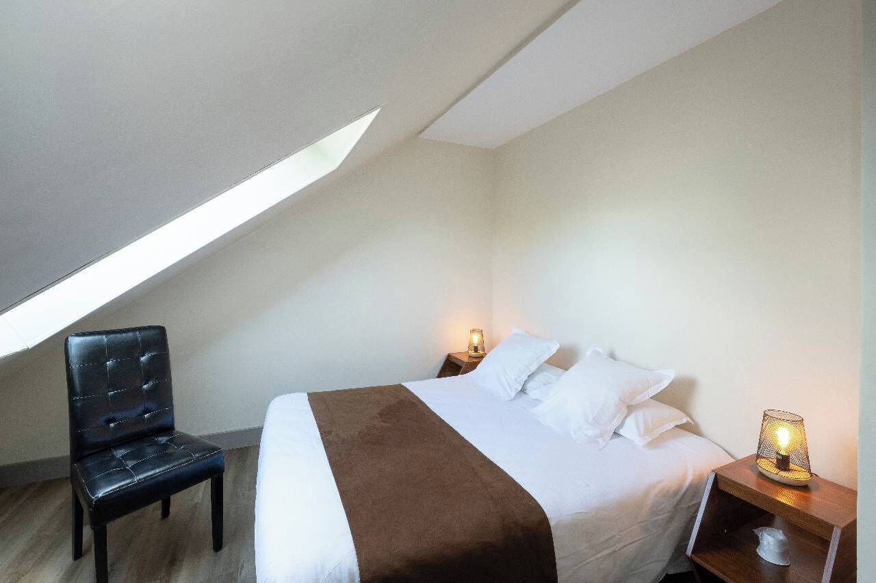 A bedroom with a bed, a chair, a nightstand, and a lamp.
