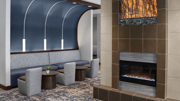 A modern lounge area with a curved seating arrangement, a fireplace, and a decorative wall with a nature-inspired mural. - Hyatt Place Boston/Braintree (Braintree)