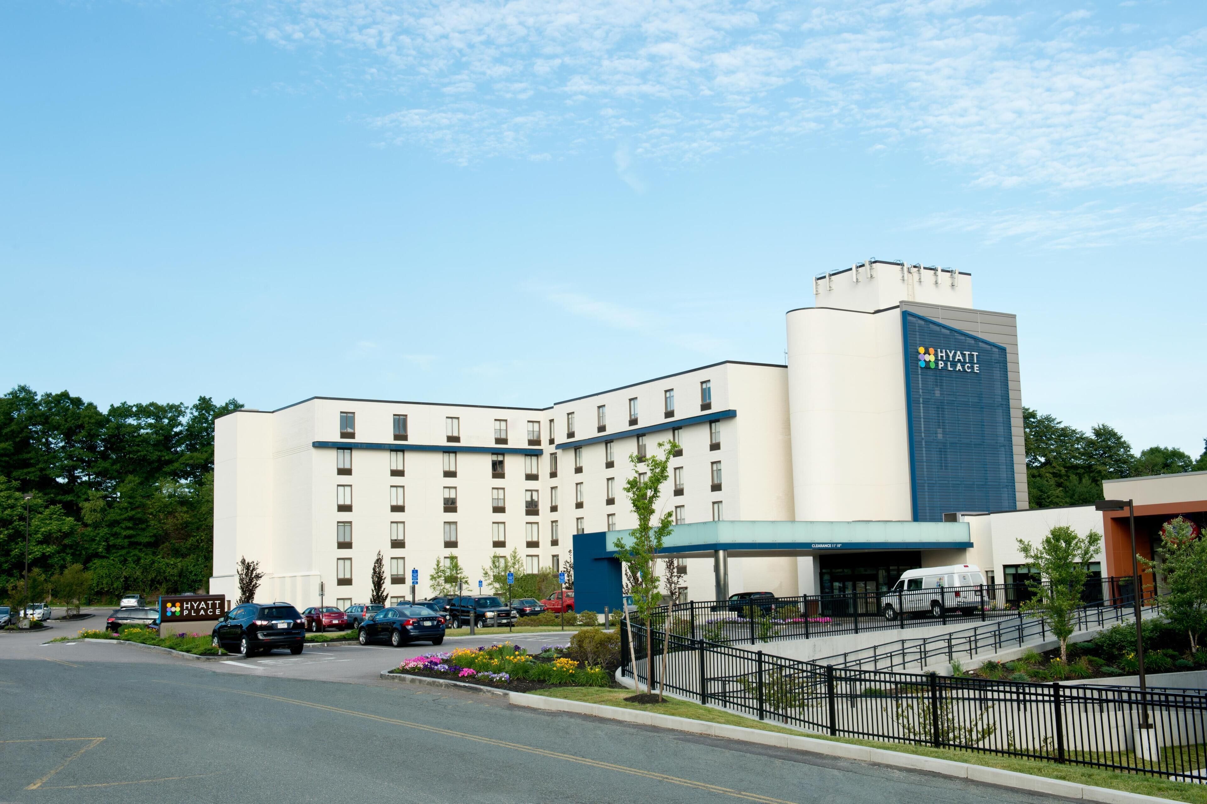 A multi-story hotel with a prominent sign, a parking lot, and a landscaped area with trees and flowers.