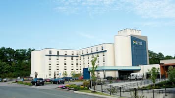 A multi-story hotel with a prominent sign, a parking lot, and a landscaped area with trees and flowers.
