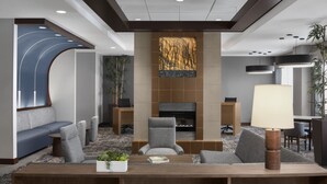 A modern lobby with a seating area, a fireplace, and a large table with a lamp. - Hyatt Place Boston/Braintree (Braintree)