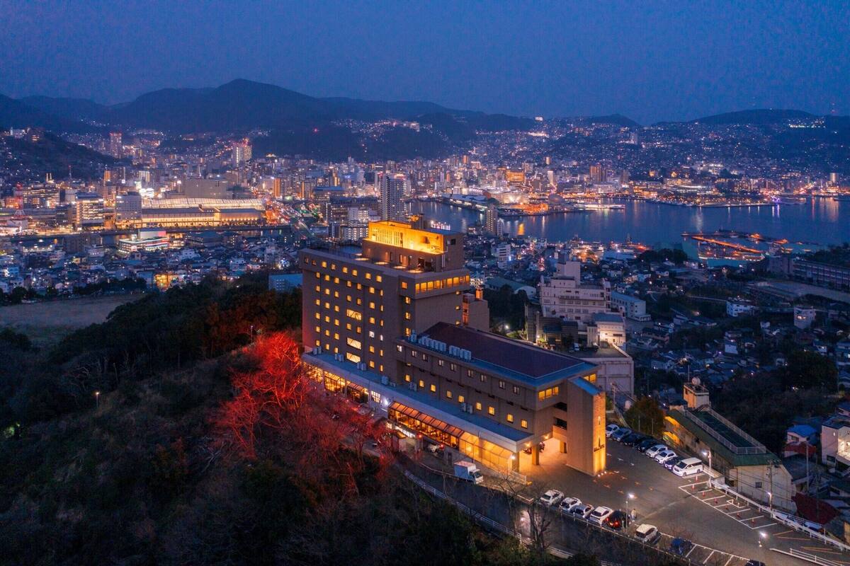 A hotel with multiple floors, a parking area, and a view of a cityscape and water body.