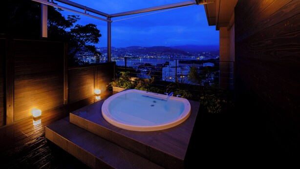 A modern bathroom with a freestanding bathtub, a view of a cityscape, and a wooden interior. - Inasayama Kanko Hotel (Nagasaki)