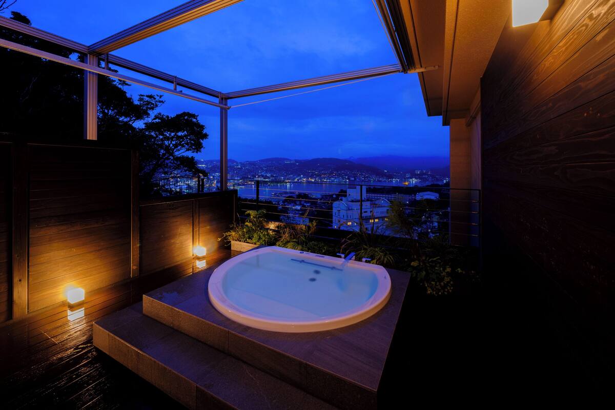 A modern bathroom with a freestanding bathtub, a view of a cityscape, and a wooden interior.