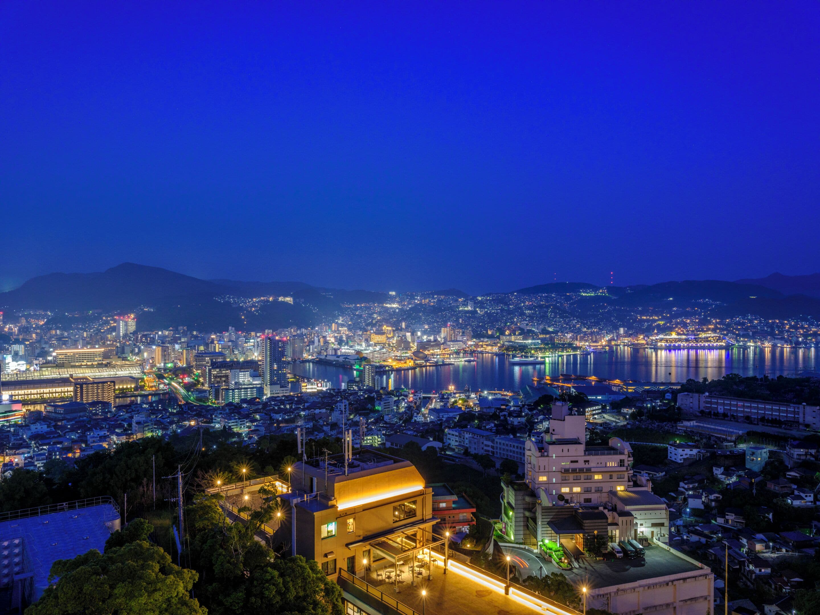 A nighttime cityscape with a prominent waterfront, illuminated buildings, and a mix of residential and commercial structures.