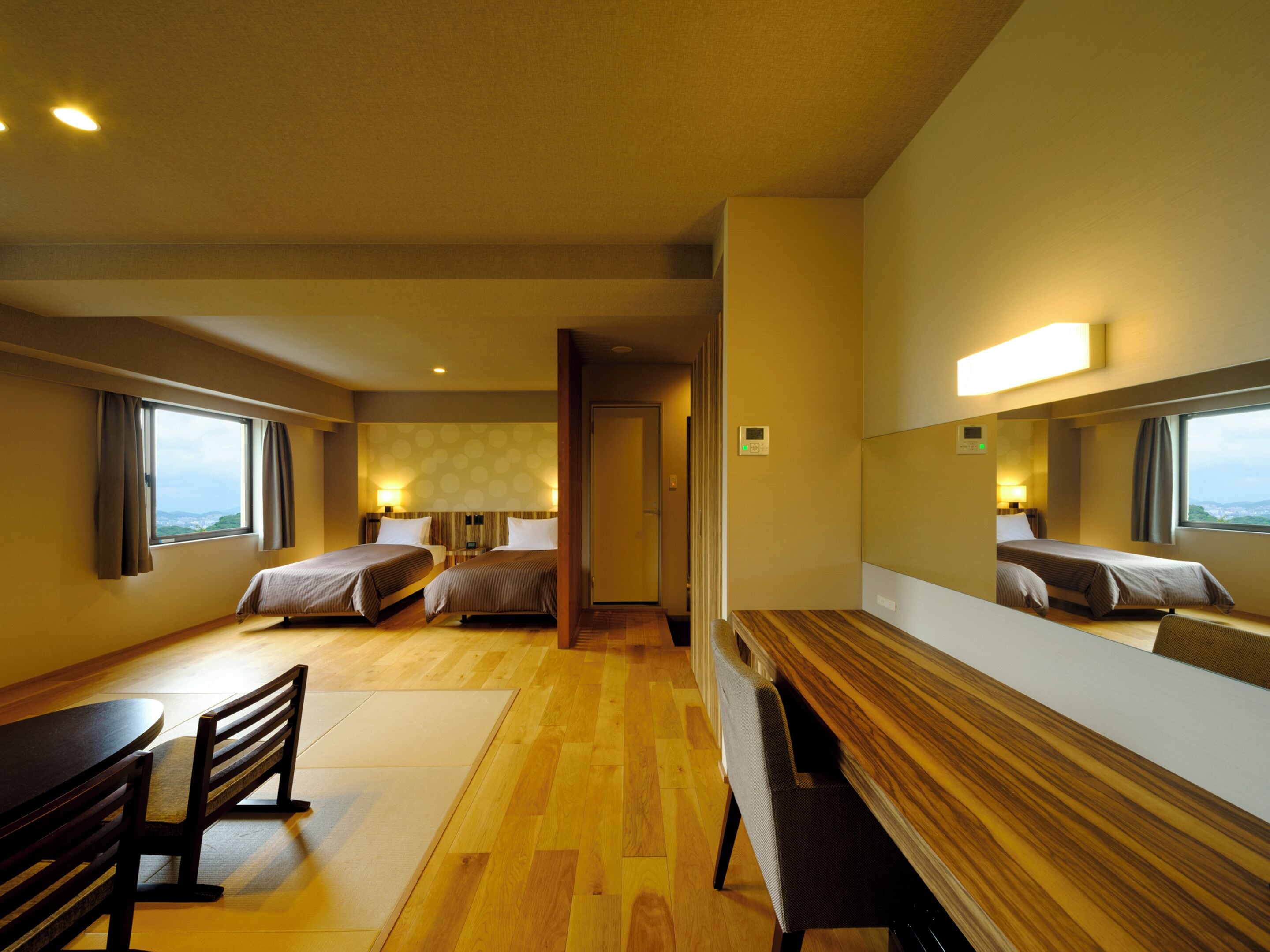 A hotel room with two beds, a wooden bench, a small table, and a large mirror.