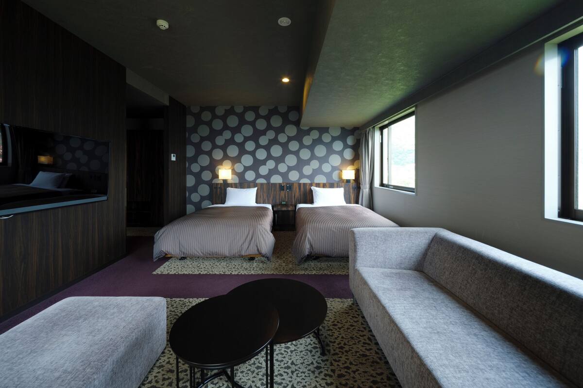A modern hotel room with a large bed, two bedside tables, a sofa, a small table, and a TV.