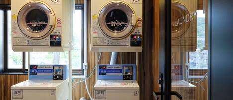 Two coin-operated laundry machines with digital displays, located in a room with wooden paneling and a window providing natural light.