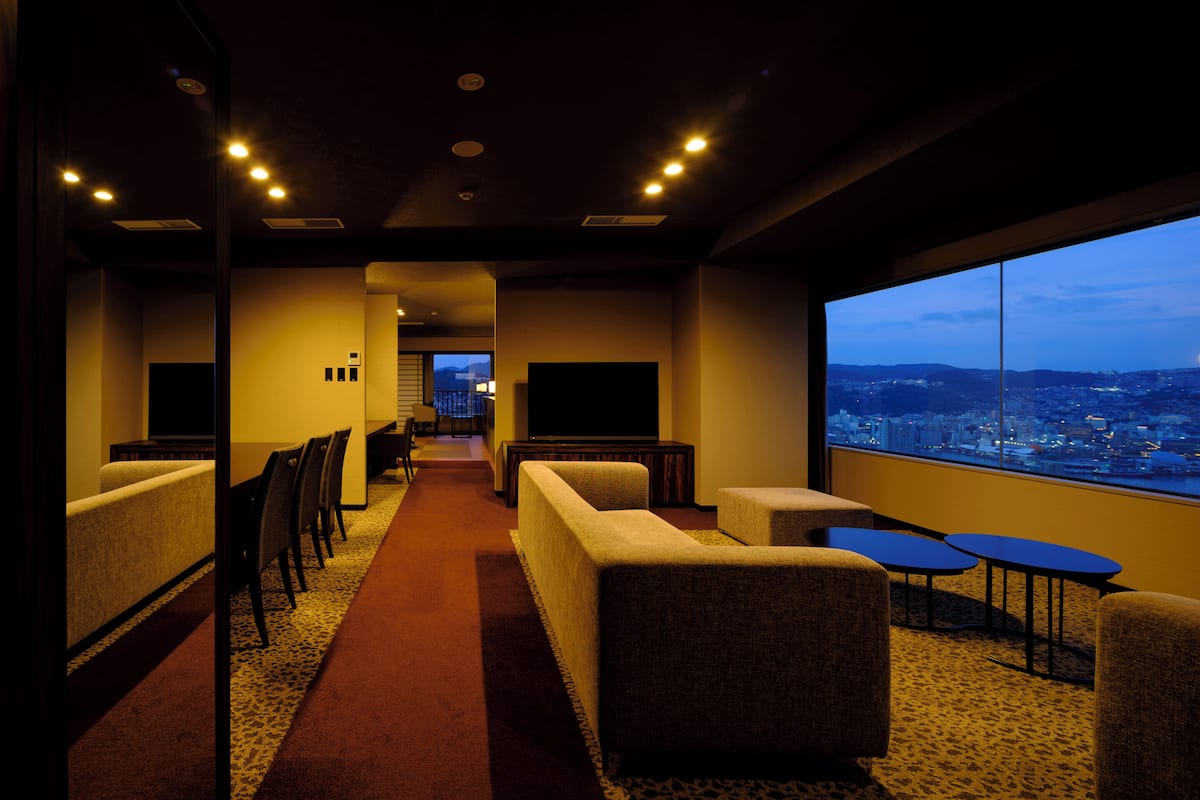 A hotel room with a city view, a seating area with sofas and chairs, and a small table.
