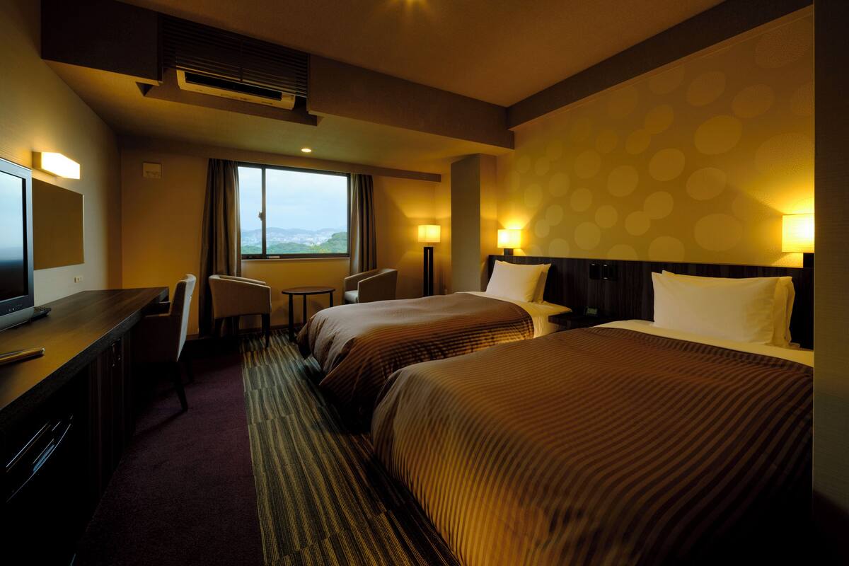 A hotel room with two beds, a desk with a TV, a chair, and a window with a view.