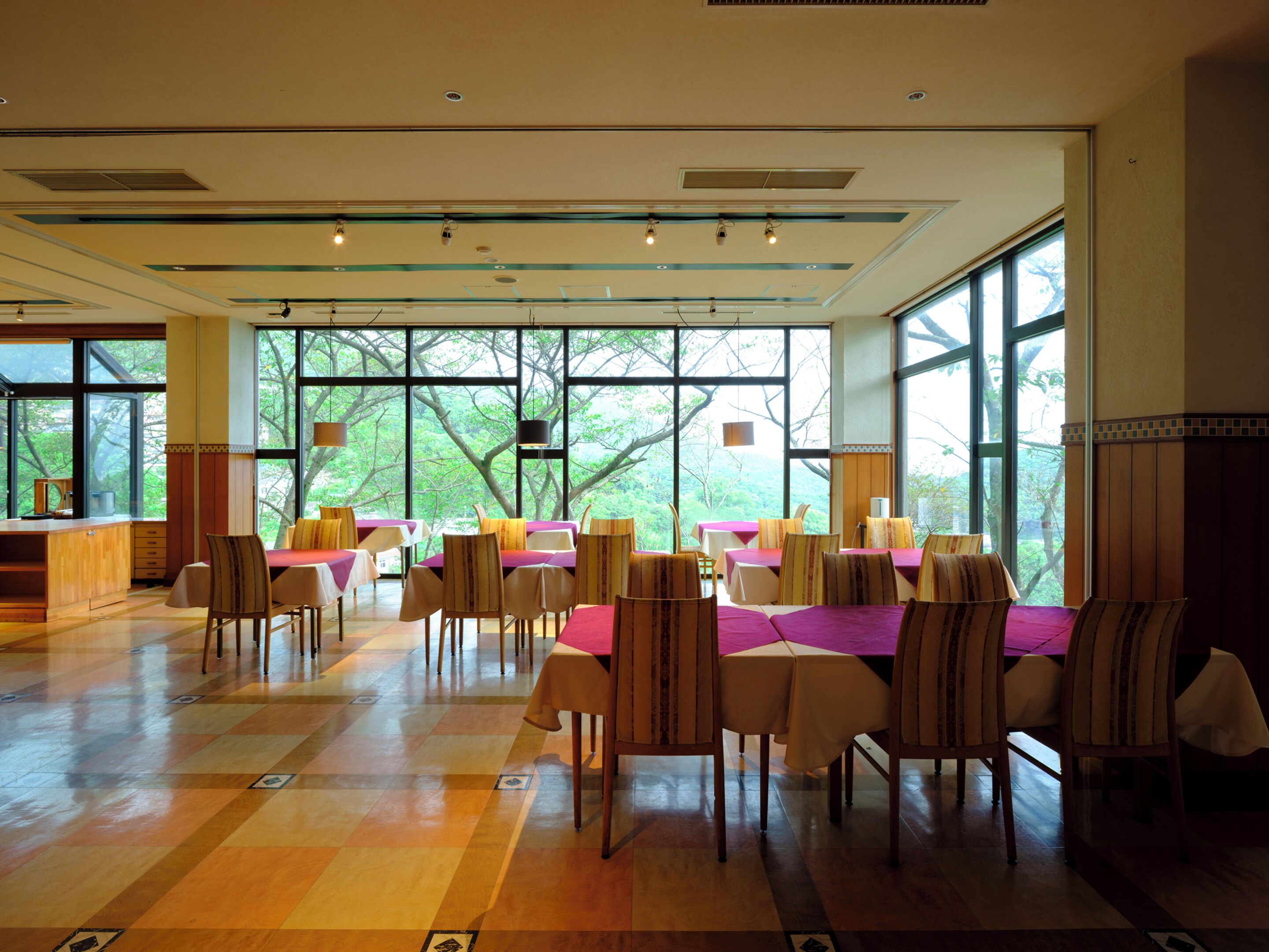 A spacious dining area with large windows, wooden flooring, and multiple tables and chairs.