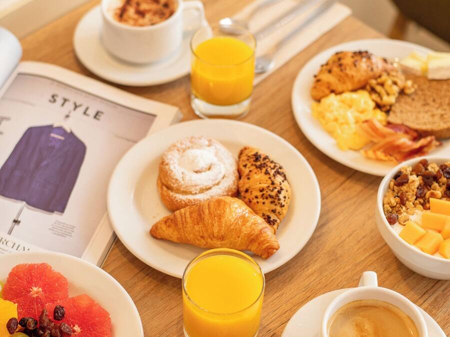 Une table de petit-déjeuner avec des assiettes remplies de nourriture, un verre de jus d’orange et une tasse de café.