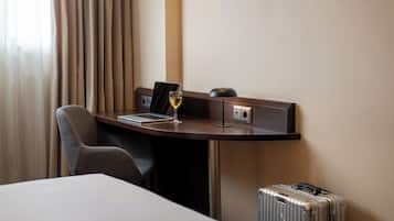 Een hotelkamer met een bureau, een laptop, een glas wijn, een koffer en een stoel.