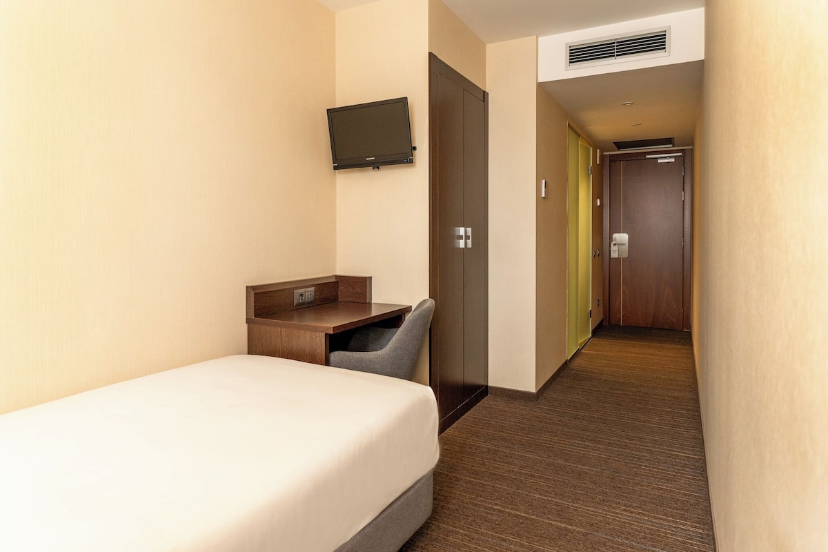 A hotel room with a bed, a desk, a chair, a television, and a door leading to another room.