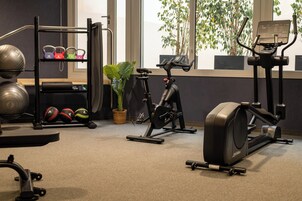 Ein Fitnessraum mit Trainingsgeräten, einem Kettlebell-Ständer und einem Blumentopf.