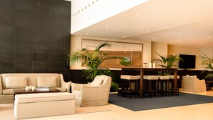 A modern hotel lobby with a sofa, ottoman, and bar area with stools. - Arco Barcelona Hotel (Barcelona)