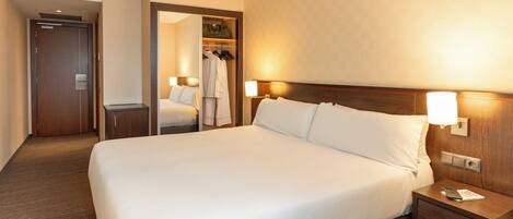 Habitación de hotel con una cama grande, lámparas de noche, cabecero de madera, mesita de noche, armario y un espejo.