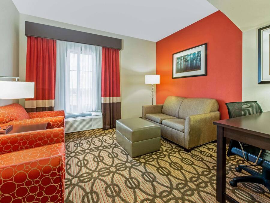 A hotel room with a sofa, ottoman, and a desk with a chair.