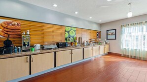 A spacious kitchen area with wooden cabinets, a countertop with various appliances, and a large poster on the wall. - La Quinta Inn & Suites by Wyndham Leesville Ft. Polk (Leesville)