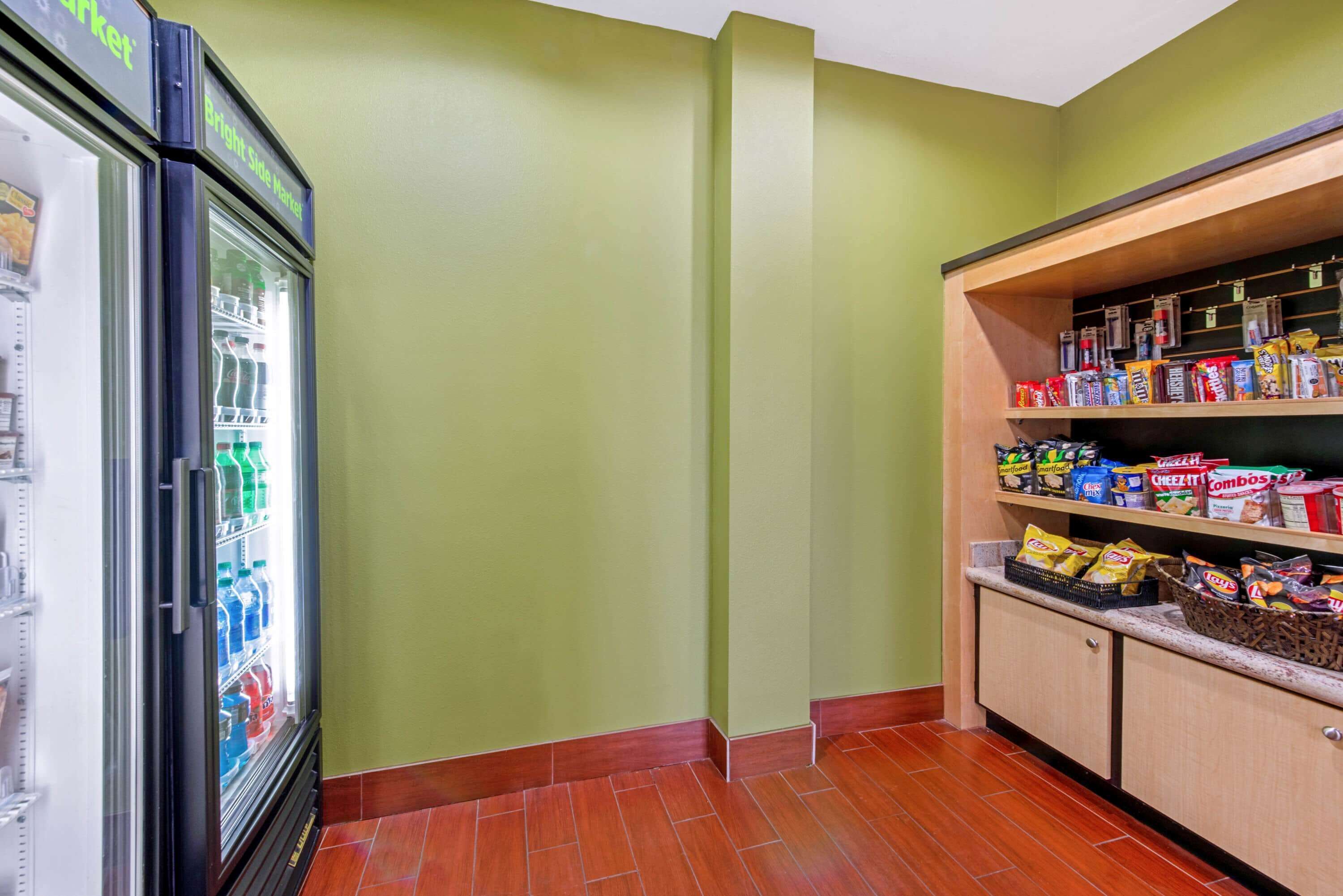 A kitchenette with a refrigerator stocked with beverages, a shelf with snacks, and a wooden cabinet with more snacks.