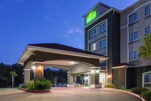 A hotel with a prominent green sign, a covered entrance, and a parking lot.