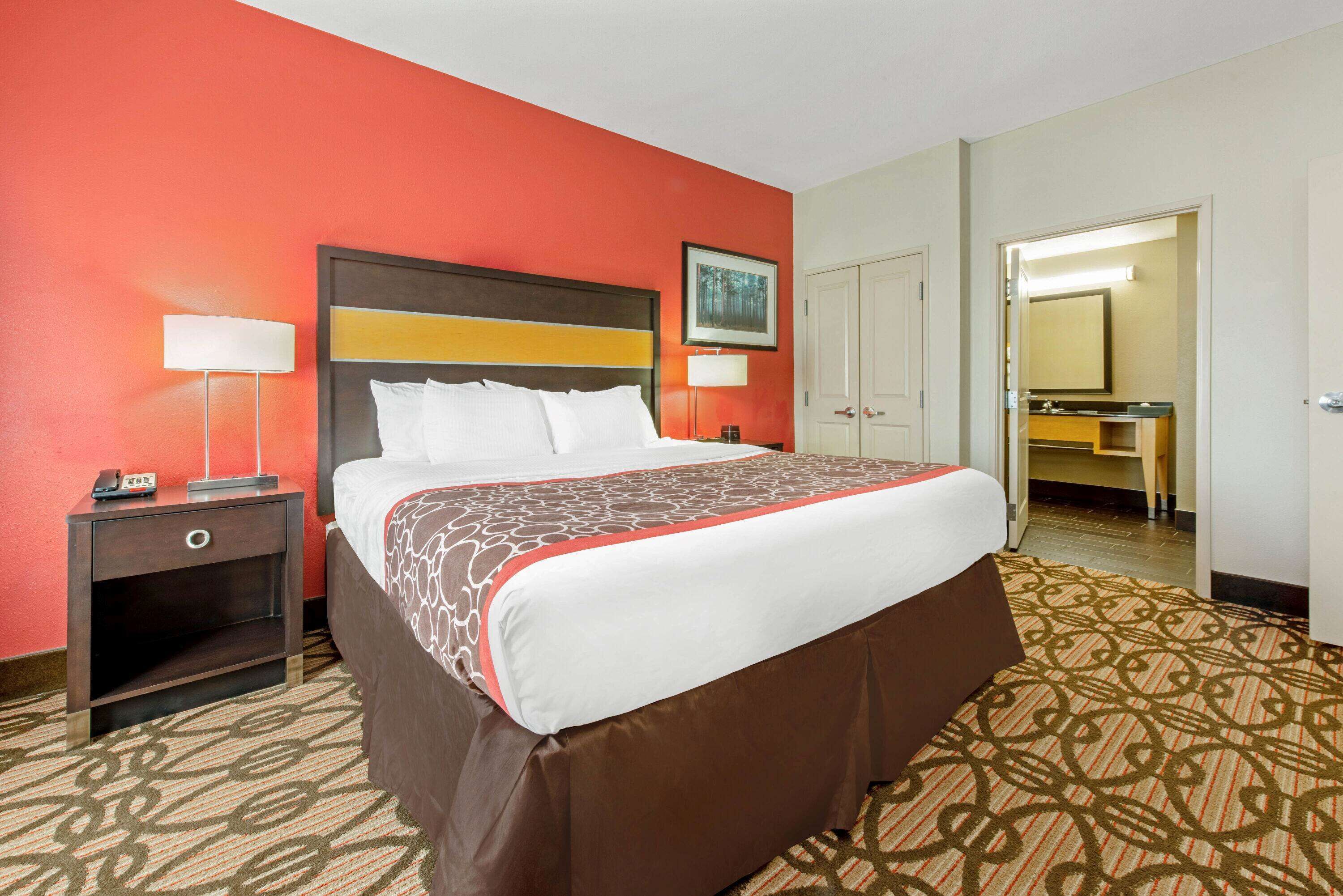 A hotel room with a large bed, a nightstand, a desk, and a bathroom visible through an open door.