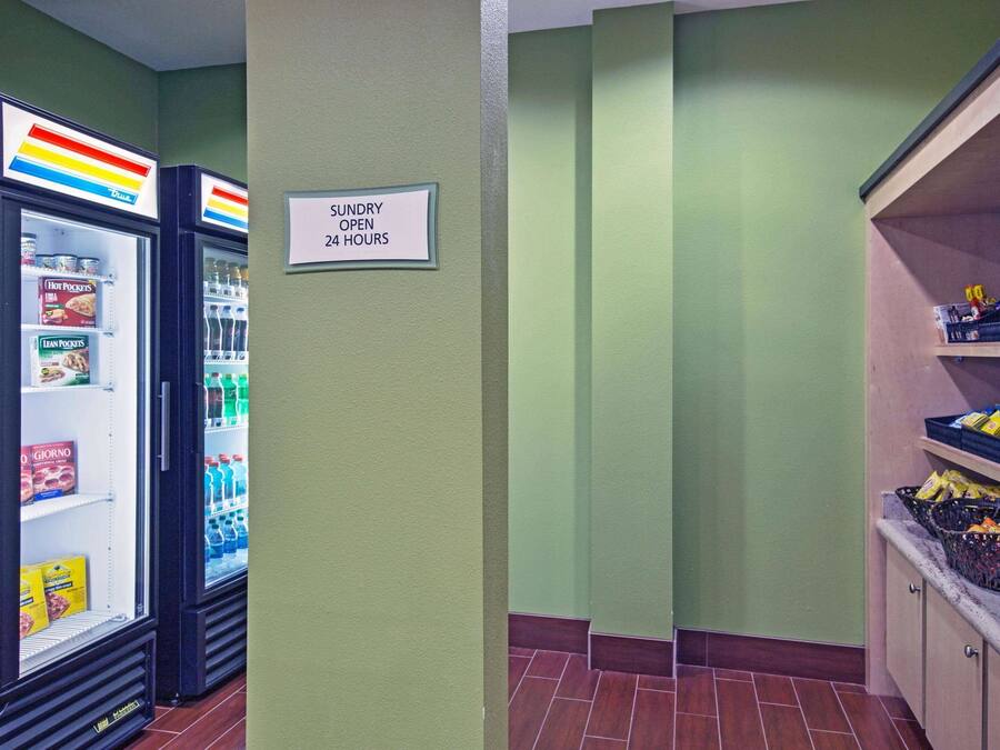 Una zona de kitchenette con dos refrigeradores llenos de alimentos y un letrero que indica que la tienda de conveniencia está abierta las 24 horas.