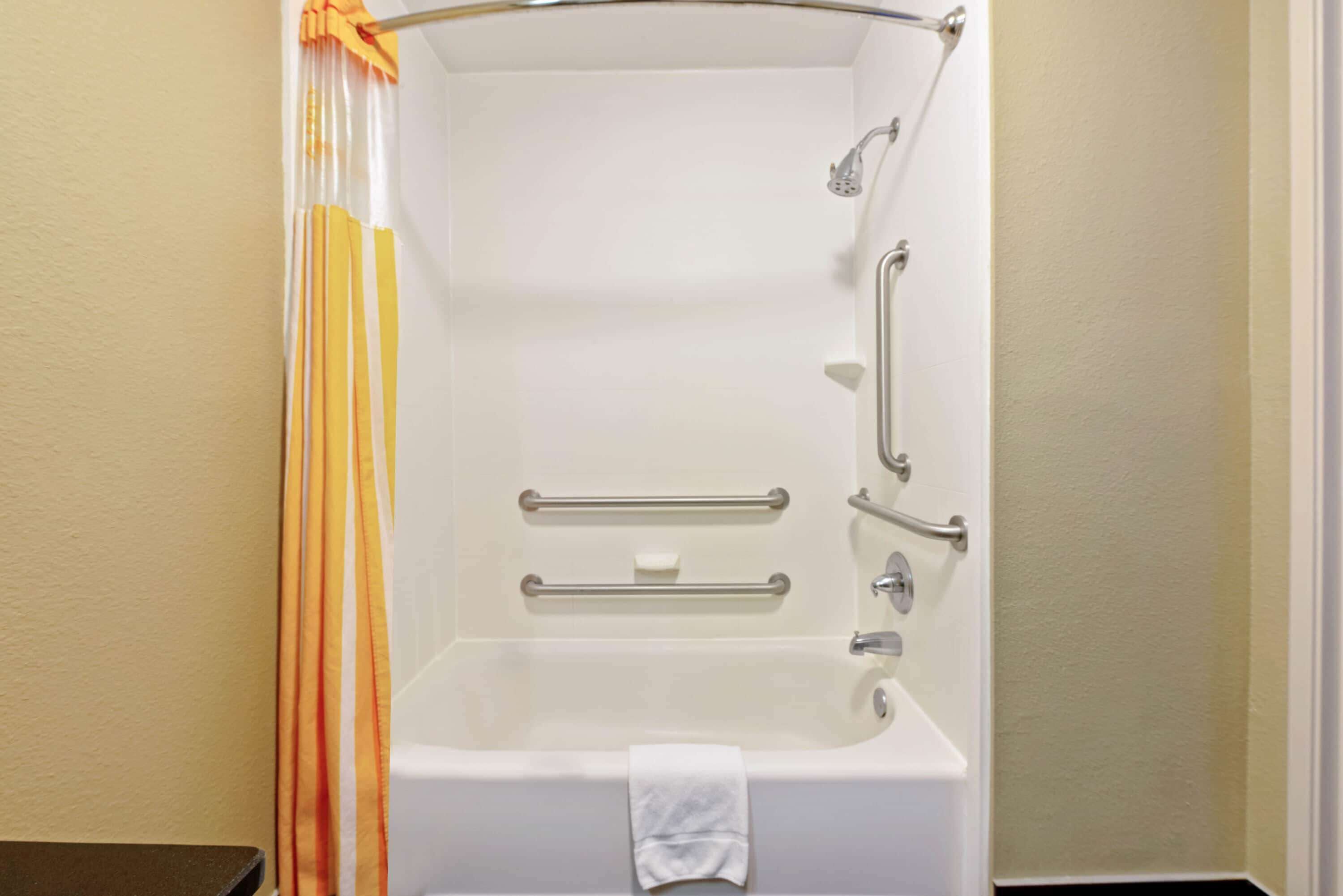 Une baignoire blanche équipée d’une pomme de douche, de barres d’appui et d’un porte-serviettes.