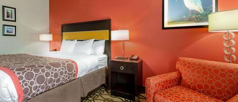 Una habitación de hotel con una cama, una mesita de noche, un sofá rojo y un cuadro de un pájaro colgado en la pared.