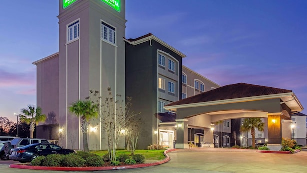 A hotel with a prominent tower featuring illuminated signage, a covered entrance, and a landscaped front yard. - La Quinta Inn & Suites by Wyndham Leesville Ft. Polk (Leesville)