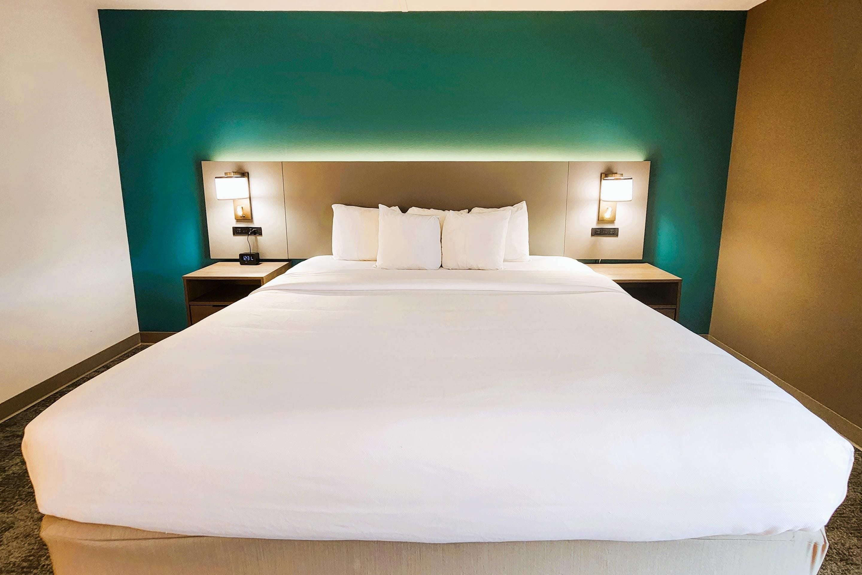 Una habitación de hotel con una cama grande, dos mesitas de noche y lámparas fijadas a la pared.