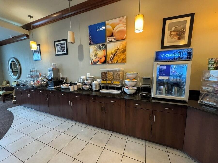 Una barra de desayuno con distintos alimentos, una máquina de café y un refrigerador que muestra un menú.
