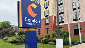 A Comfort Inn & Suites sign with a blue and yellow logo, surrounded by a well-maintained lawn and a brick building in the background.