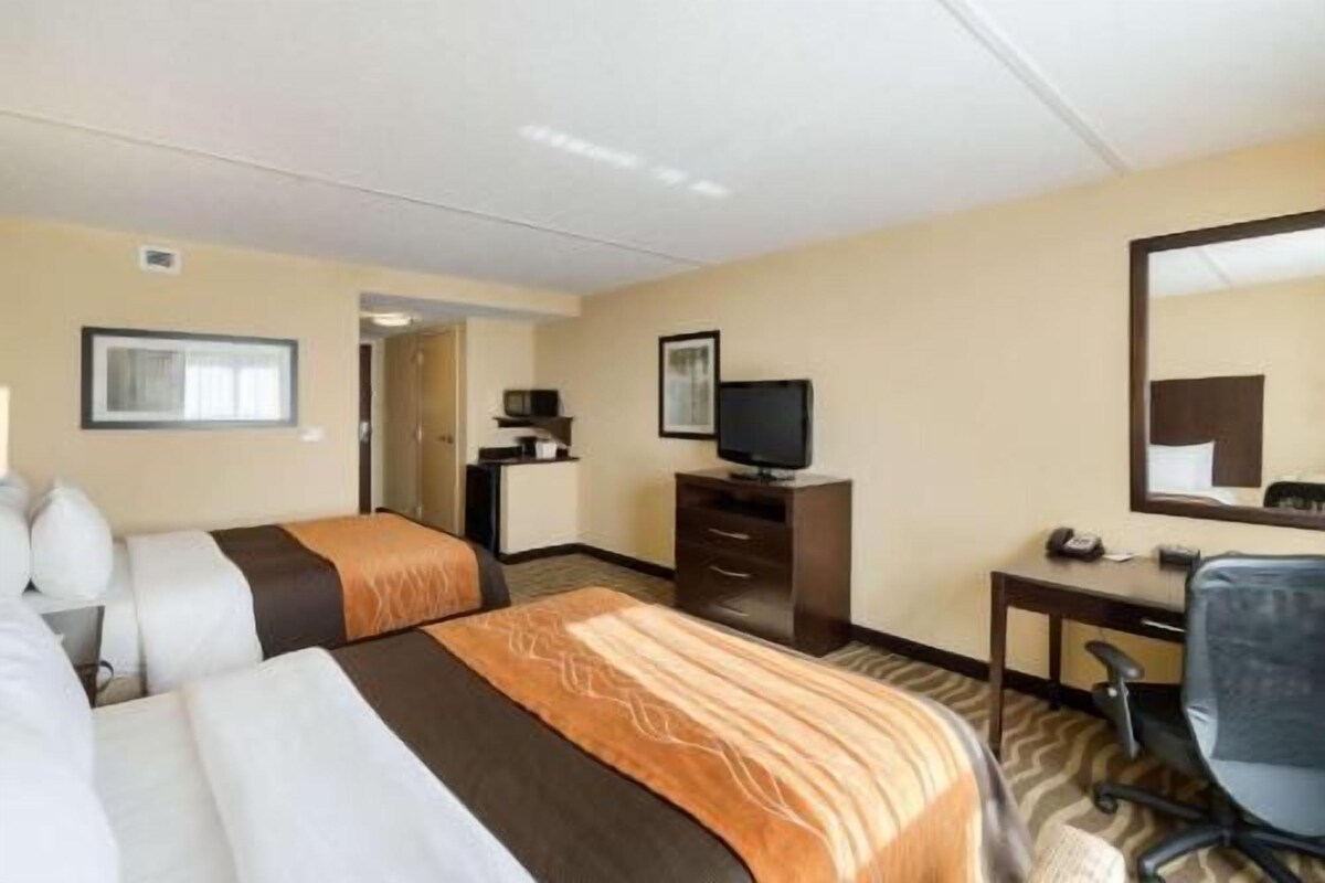 A hotel room with two beds, a desk, a television, and a mirror.