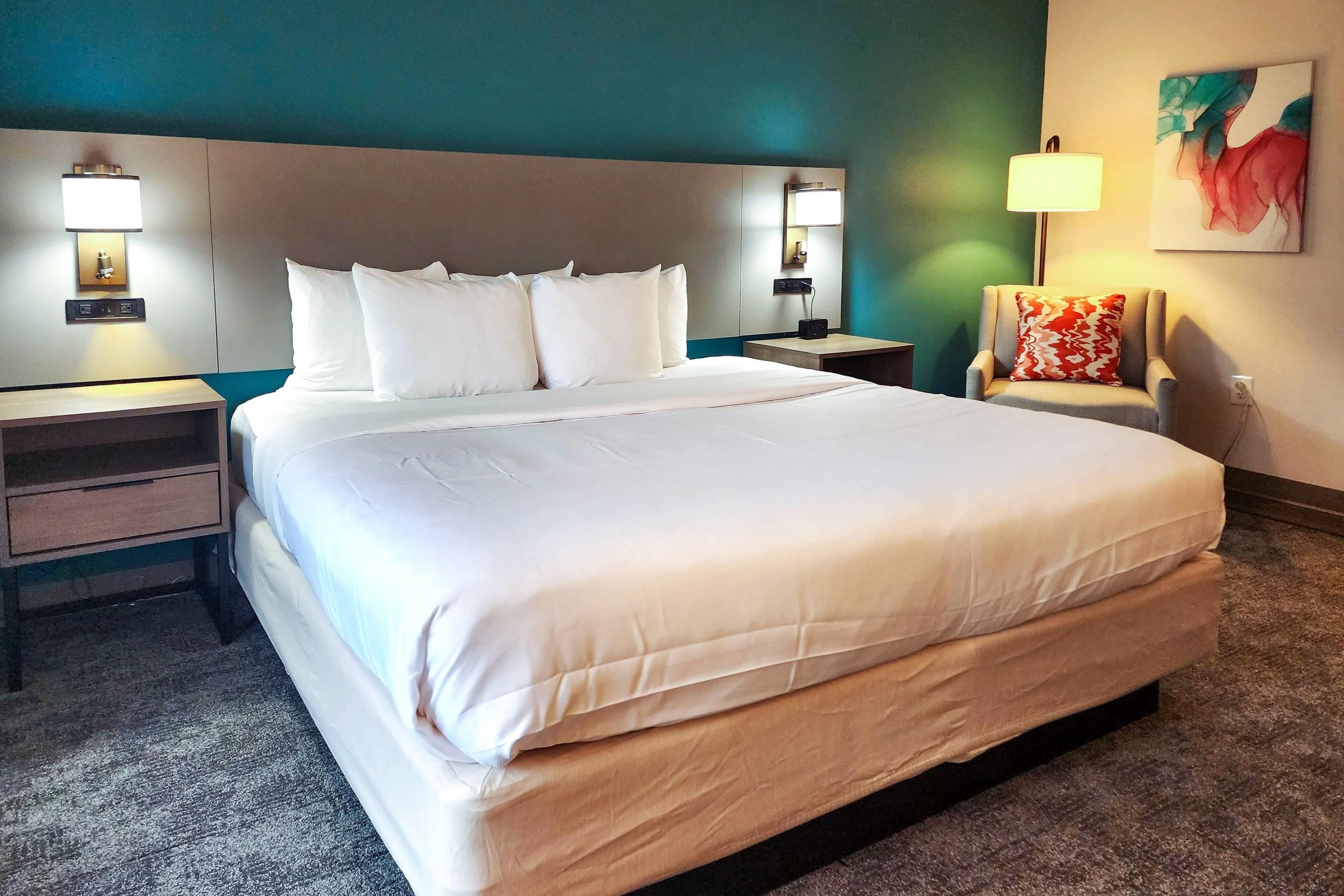 Una habitación de hotel con una cama grande, mesitas de noche, una silla y una lámpara fijada a la pared.