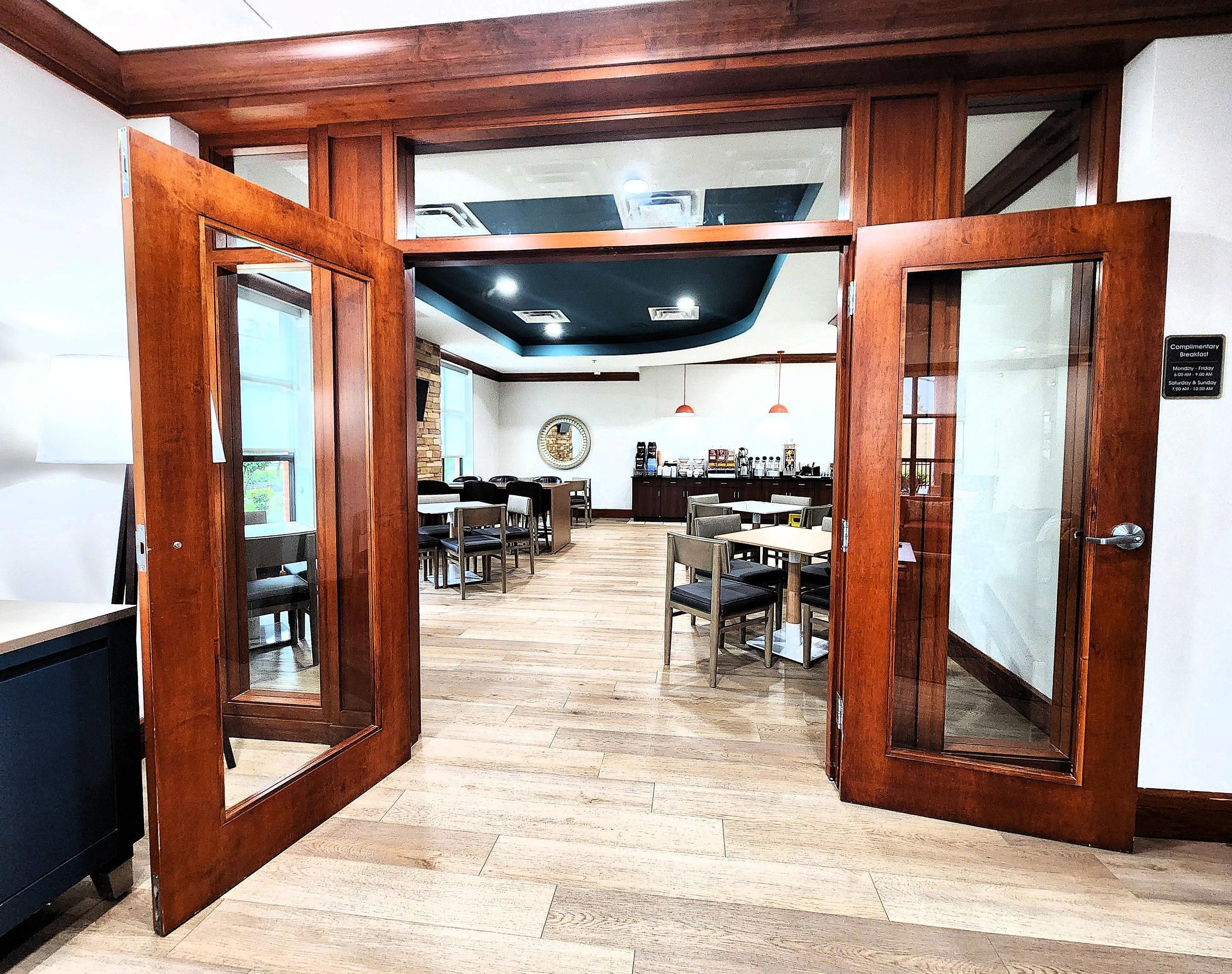 Un vestíbulo de hotel con puertas de madera, un mostrador de recepción y un área de descanso con mesas y sillas.