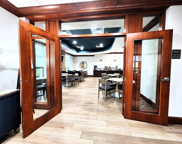 A hotel lobby with wooden doors, a reception desk, and a seating area with tables and chairs.