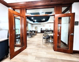 A hotel lobby with wooden doors, a reception desk, and a seating area with tables and chairs.